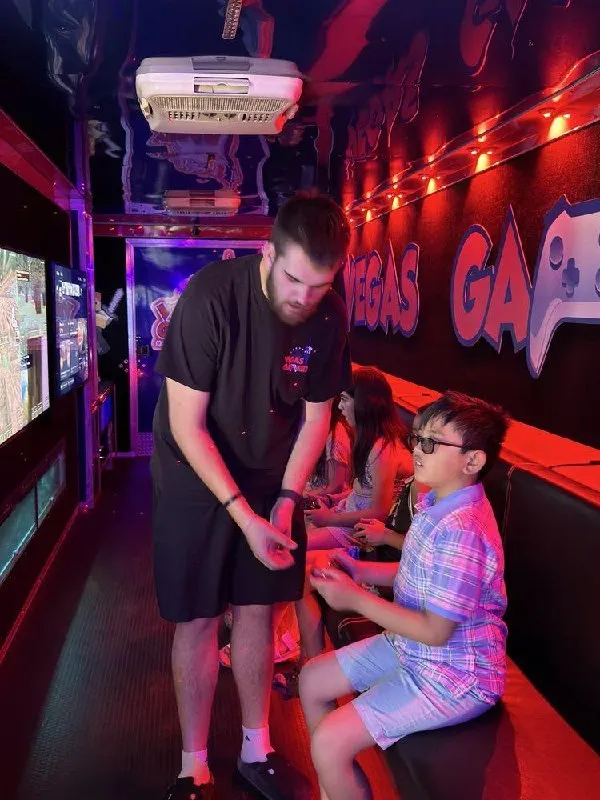 A Vegas Gamerz Game Coach crouching to help a young player with his controller inside the trailer