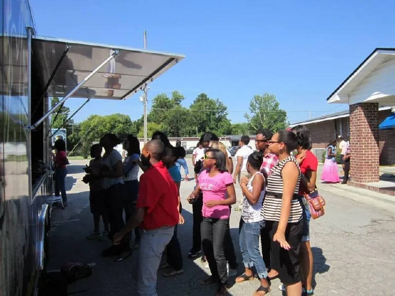 A neighborhood crowd gathered under the trailer’s awning at a block party