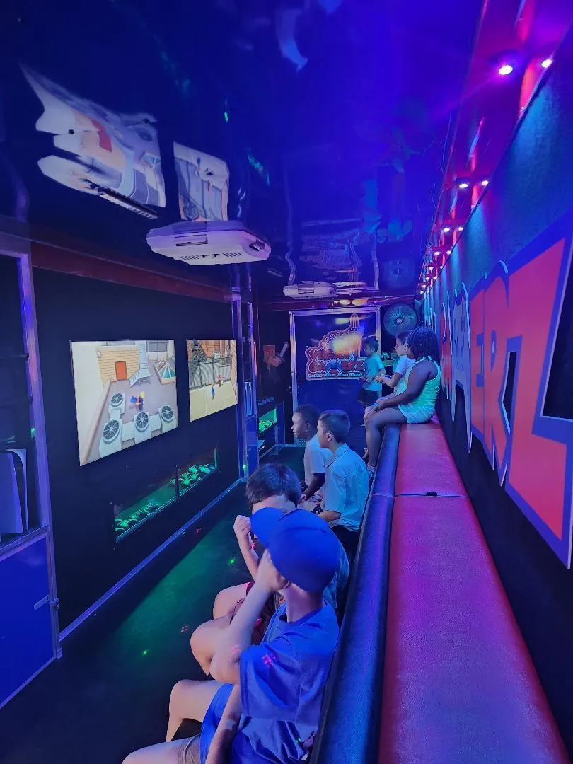 Kids seated along the trailer’s cushioned stadium bench under blue and purple lighting