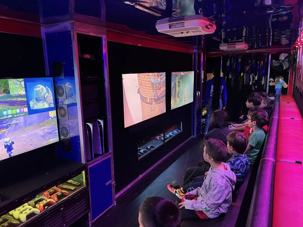 PlayStation 5 consoles and rows of controllers in the trailer’s lit equipment cabinets